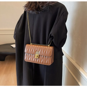 Detailed view of brown quilted leather crossbody bag with gold chain strap on model