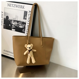 Detailed close-up of a brown tote bag featuring a cute cream knit bear pendant