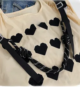 Detail view of large beige tote bag with black heart embroidery and woven straps