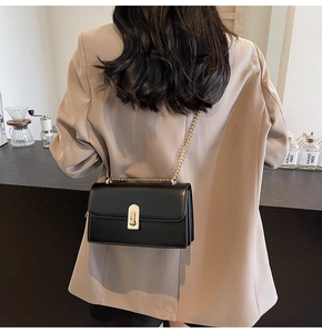Close-up of black leather rectangular shoulder bag with gold hardware on a beige blazer