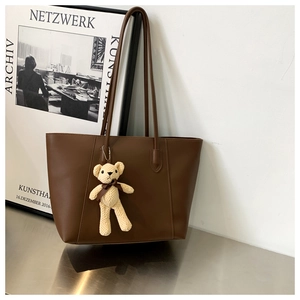 Detail of dark brown leather tote bag with a cream knitted bear charm and thin shoulder straps