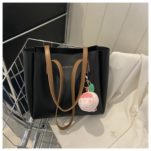 Detail of black tote bag with brown straps and peach plush charm in a shopping cart