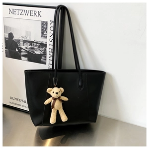 Detail of a large black tote bag with a cute cream-colored knit bear charm accessory