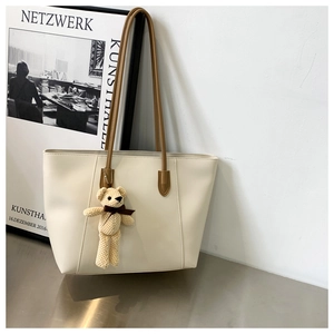 Detail of minimalist cream tote bag featuring brown straps and a plush bear charm