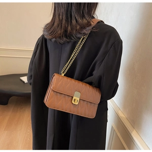 Detail of brown quilted crossbody bag with golden chain strap and rectangular turn-lock
