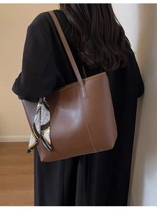 Brown leather tote bag with silk scarf accessory worn by a model in a black coat