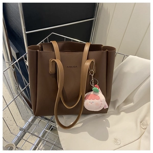 Close-up of a large brown leather tote bag in a metal basket with a pink plush charm