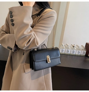 Detail of minimalist black rectangle shoulder bag with gold metal twist lock and chain strap