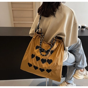 Detail of yellow drawstring tote bag with black heart mesh patch and woven handle
