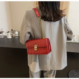 Detail of red quilted crossbody bag with gold chain strap and metallic twist lock