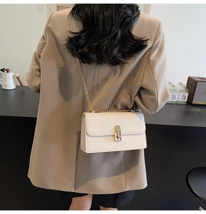 Detail of minimalist cream leather crossbody bag featuring a golden twist lock on the flap