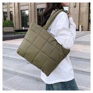 Détail du sac fourre-tout matelassé vert foncé montrant le tissu et la large bandoulière