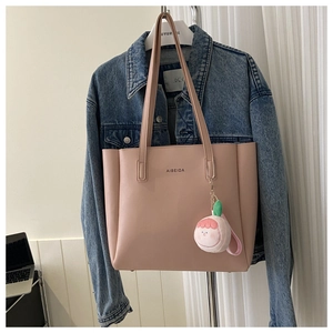 Close-up of nude pink faux leather tote bag with long straps and a cute plush charm