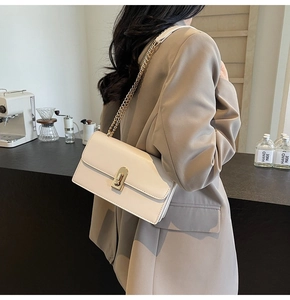 Detail of cream flap crossbody bag showing the golden twist lock and metal chain strap
