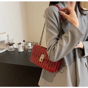 Close-up of red quilted crossbody bag with gold chain strap and wave-pattern stitching