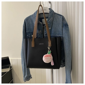 Detail of a large black matte tote bag with brown straps and a pink plush charm