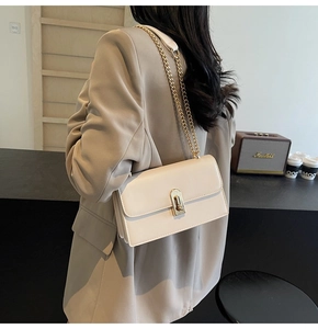 Detailed view of beige leather crossbody bag with gold chain strap and turn-lock closure