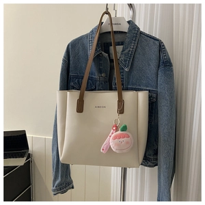 Detail of cream tote bag with brown straps and pink plush pendant on a hanger