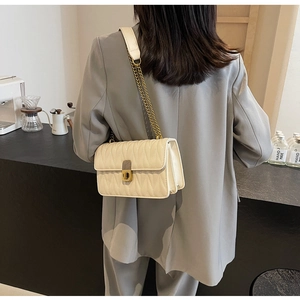 Detail of cream quilted crossbody bag featuring a gold twist lock and chain strap