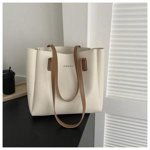 Close-up of a cream tote bag with brown leather straps and branded logo on the front
