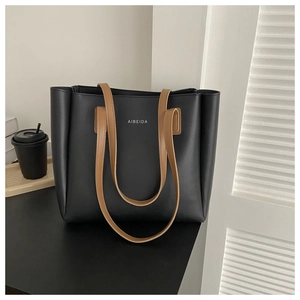 Detail of minimalist black tote bag with brown straps and white logo on a desk