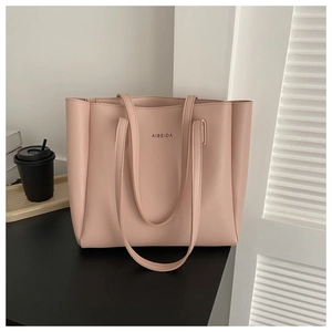 Detail shot of a light pink PU leather tote bag with brand logo on a modern desk
