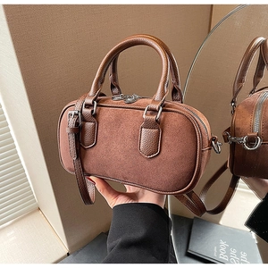 Detailed close-up of brown suede Boston bag with leather handles and silver hardware