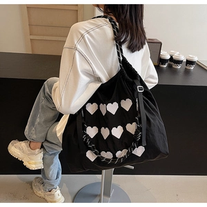 Detail of black tote bag with pixel heart embroidery and braided strap on model
