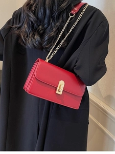 Red flap shoulder bag with gold chain strap and metallic clasp worn over a black coat