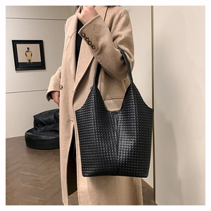 Sac fourre-tout noir tressé porté par un mannequin en manteau long couleur chameau