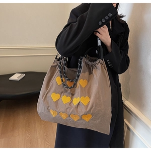 Detailed view of brown quilted tote bag with yellow heart embroidery and woven straps