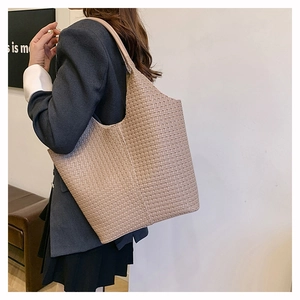 Détail de la texture tressée et de la large bandoulière d'un sac cabas beige sur un mannequin