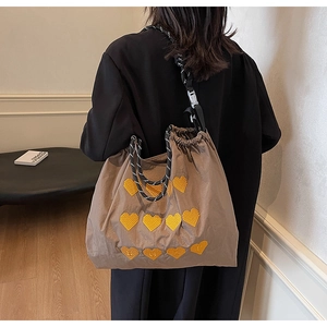 Detail of a brown drawstring tote bag featuring yellow heart patterns and woven rope straps