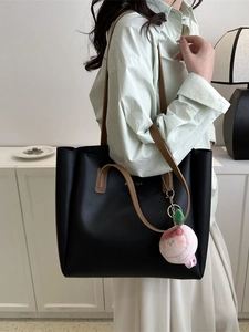 Minimalist black oversized tote bag with brown straps and pink plush charm accessory