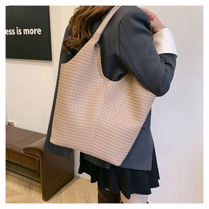 Gros plan détaillé d'un grand sac cabas tissé beige porté à l'épaule par un mannequin