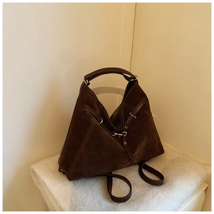Detail of a large dark brown suede tote bag with leather straps and metal buckle accents