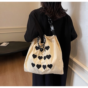 Detail of beige drawstring tote bag with black heart embroidery and woven shoulder strap