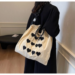 Detail of cream drawstring tote bag featuring black heart patches and braided rope strap