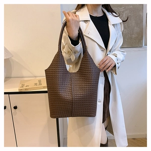 Détail d'un sac cabas tressé marron foncé porté avec un trench-coat blanc chic