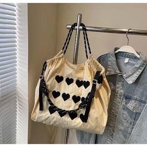 Detail of beige large tote bag with black 3D heart patches and rope handles