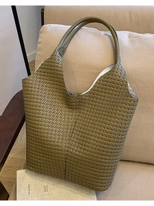 Sac cabas en cuir tressé vert olive avec poignées minimalistes sur un canapé beige