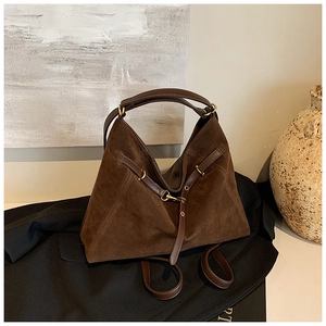 Detail view of deep brown suede tote with vintage gold buckles on a premium texture