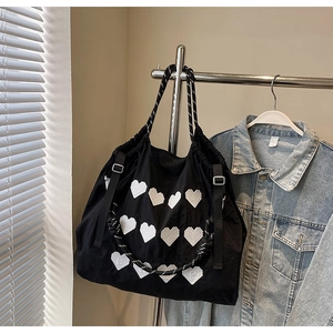 Close-up of black nylon tote bag with heart embroidery and woven handles on hanger