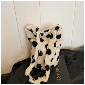 Detailed view of white fluffy tote bag with black cow spots on a leather jacket background