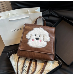 Detail view of a vintage brown leather backpack with a plush white cartoon dog on the flap