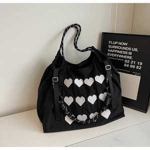 Detail of black nylon tote bag featuring white heart embroidery and thick rope handles