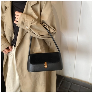 Side view of a black matte leather baguette shoulder bag with gold clasp on a trench coat