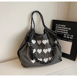 Detail of grey tote bag with heart patterns and woven rope handles on a white surface