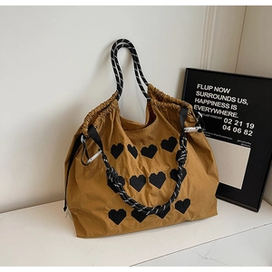 Detail of khaki nylon tote bag featuring black heart patches and woven rope handles