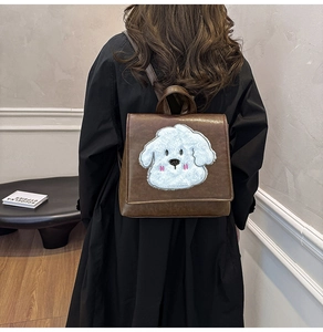 Rear view of brown leather backpack featuring a white plush dog face design on the flap